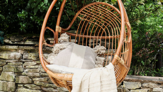 Rattan hanging egg swing chair outside with cushion and throw.