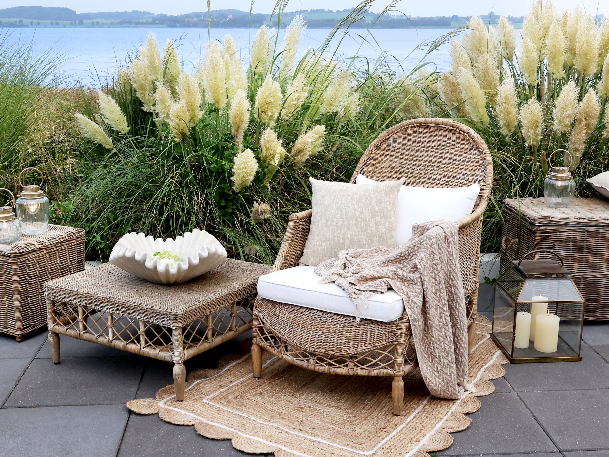 An outdoor living space with rattan furniture, lanterns a jute rug and pampas grass.