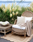 An outdoor living space with rattan furniture, lanterns a jute rug and pampas grass.