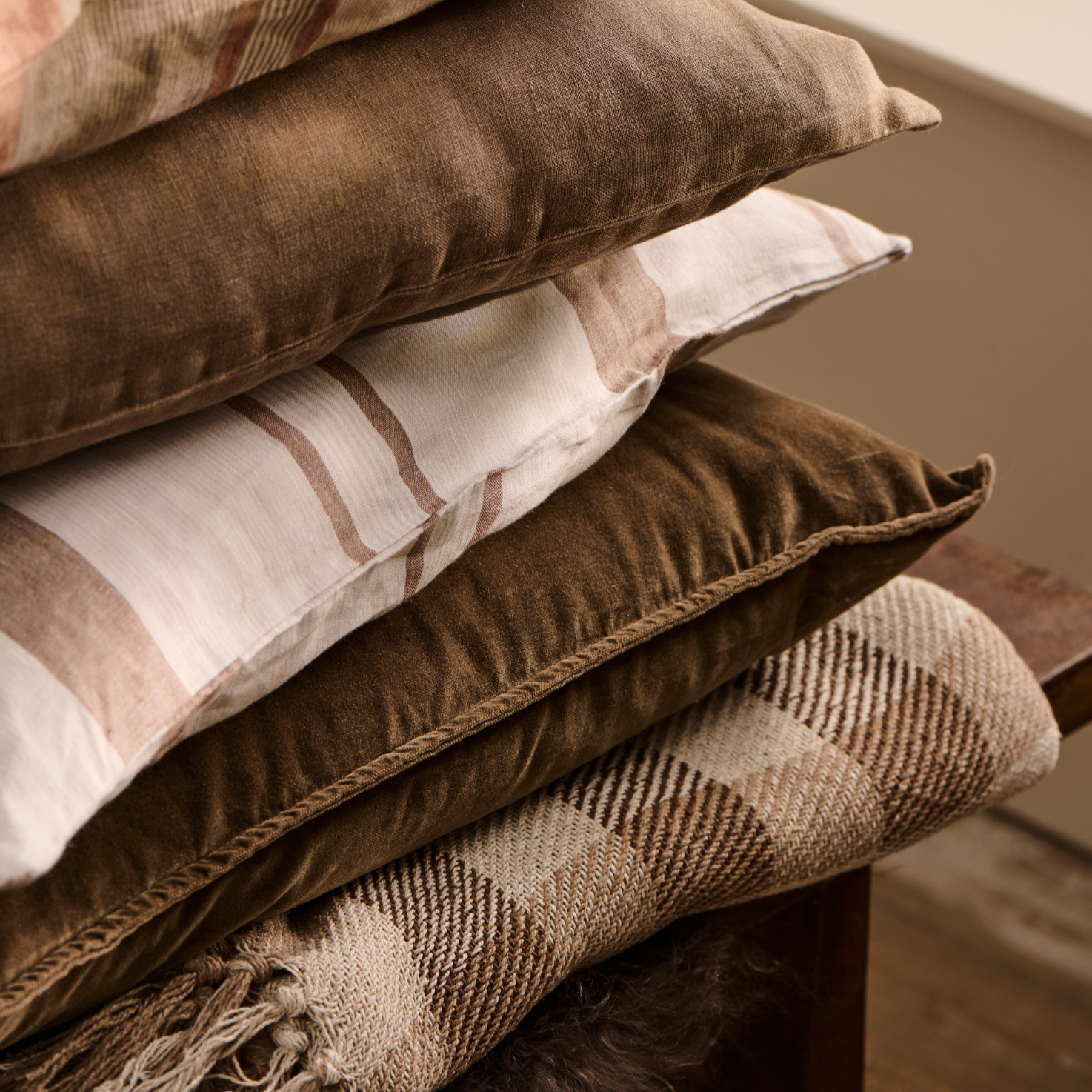 Pile of neutral cushions and throws, with checked natural throw at the bottom.