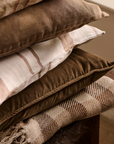 Pile of neutral cushions and throws, with checked natural throw at the bottom.