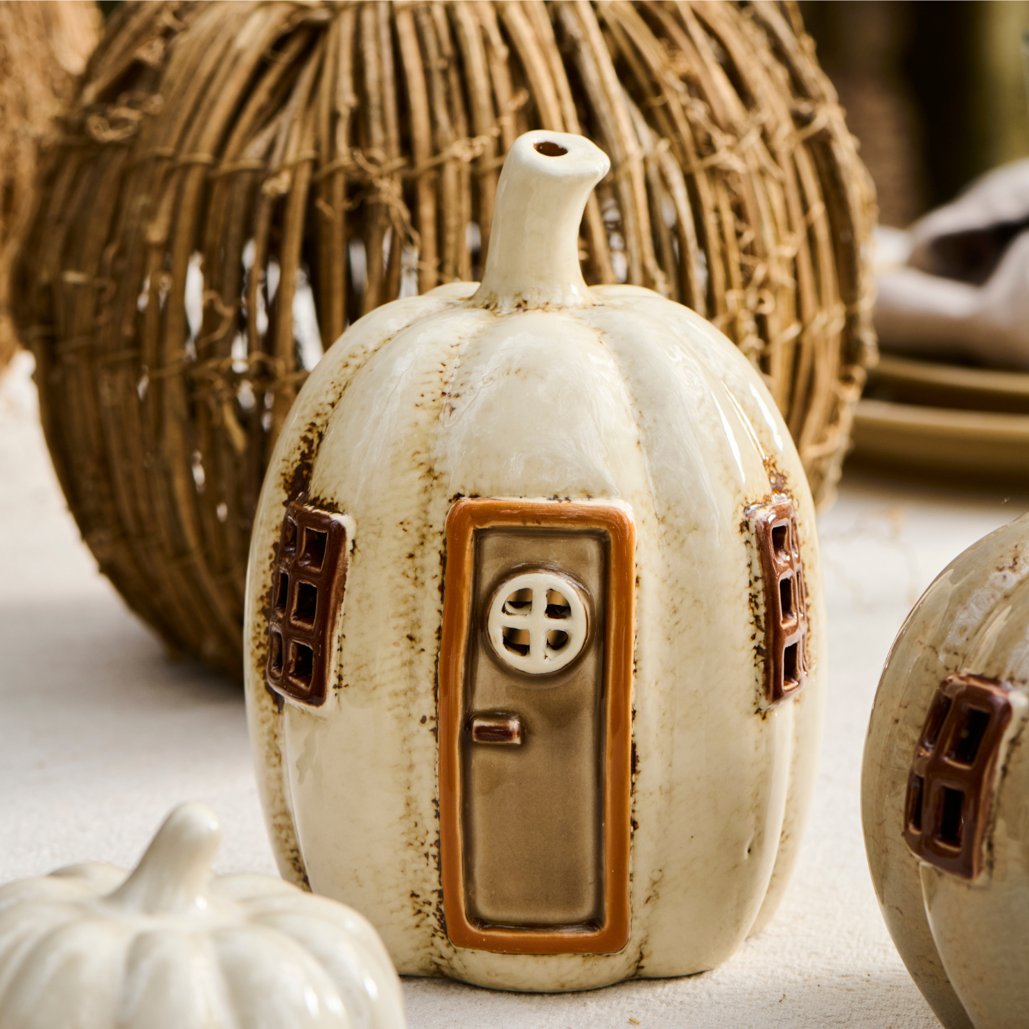 Pumpkin shaped ceramic tea light holder on table with other fall decorations.