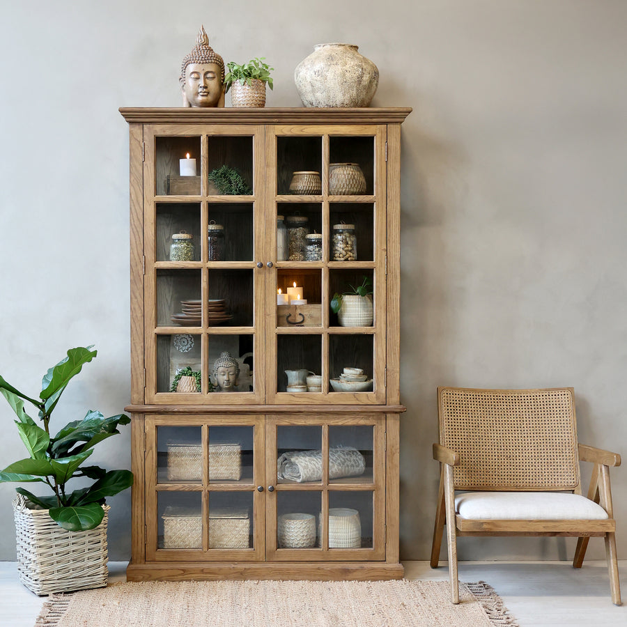 Natural wooden armoire with home decor in a neutral room with a plan and chair.