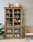 Natural wooden armoire with home decor in a neutral room with a plan and chair.