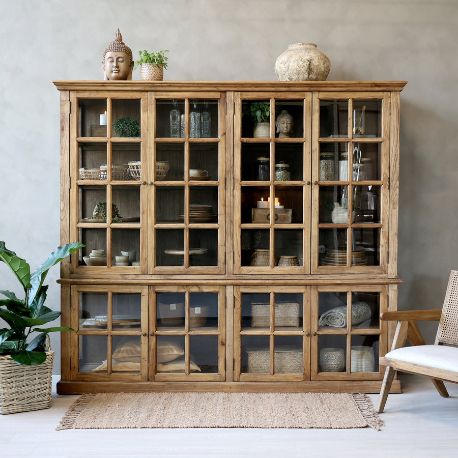 large wooden armoire displaying home decor in neutral living room with plant and rug.