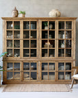 large wooden armoire displaying home decor in neutral living room with plant and rug.