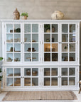 Large white armoire cabinet with glass doors filled with home decor.