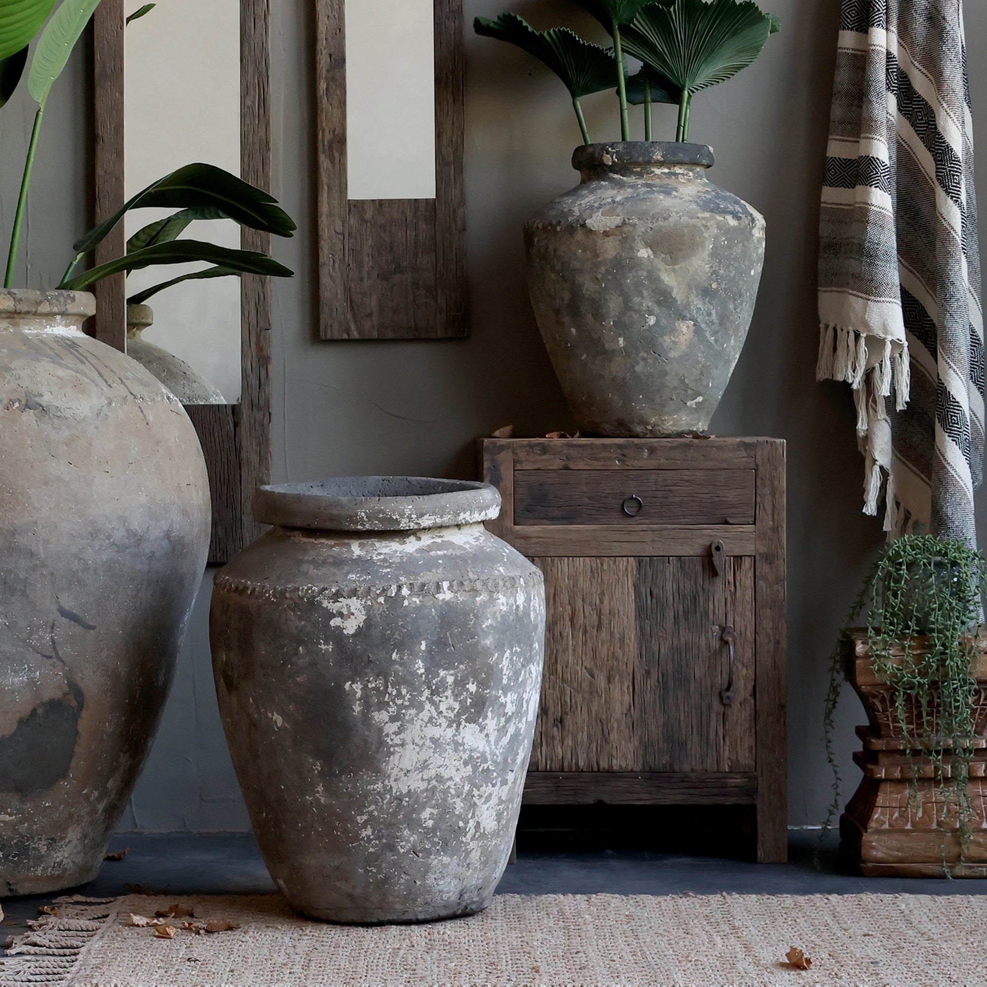 Reclaimed wooden cabinet with one drawer and one door, styled with large plant pots, mirrors and textiles.