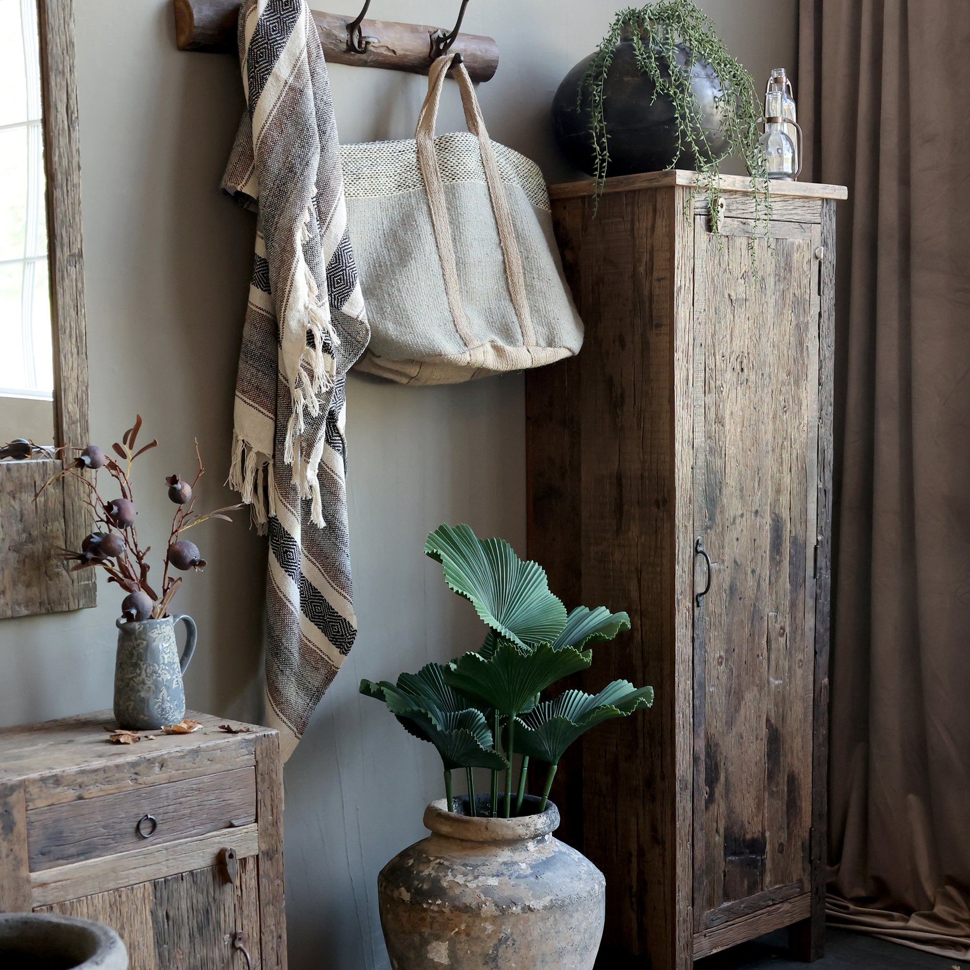 Tall reclaimed wooden cabinet styled with plants, textiles and other wooden furniture pieces.