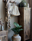 Tall reclaimed wooden cabinet styled with plants, textiles and other wooden furniture pieces.