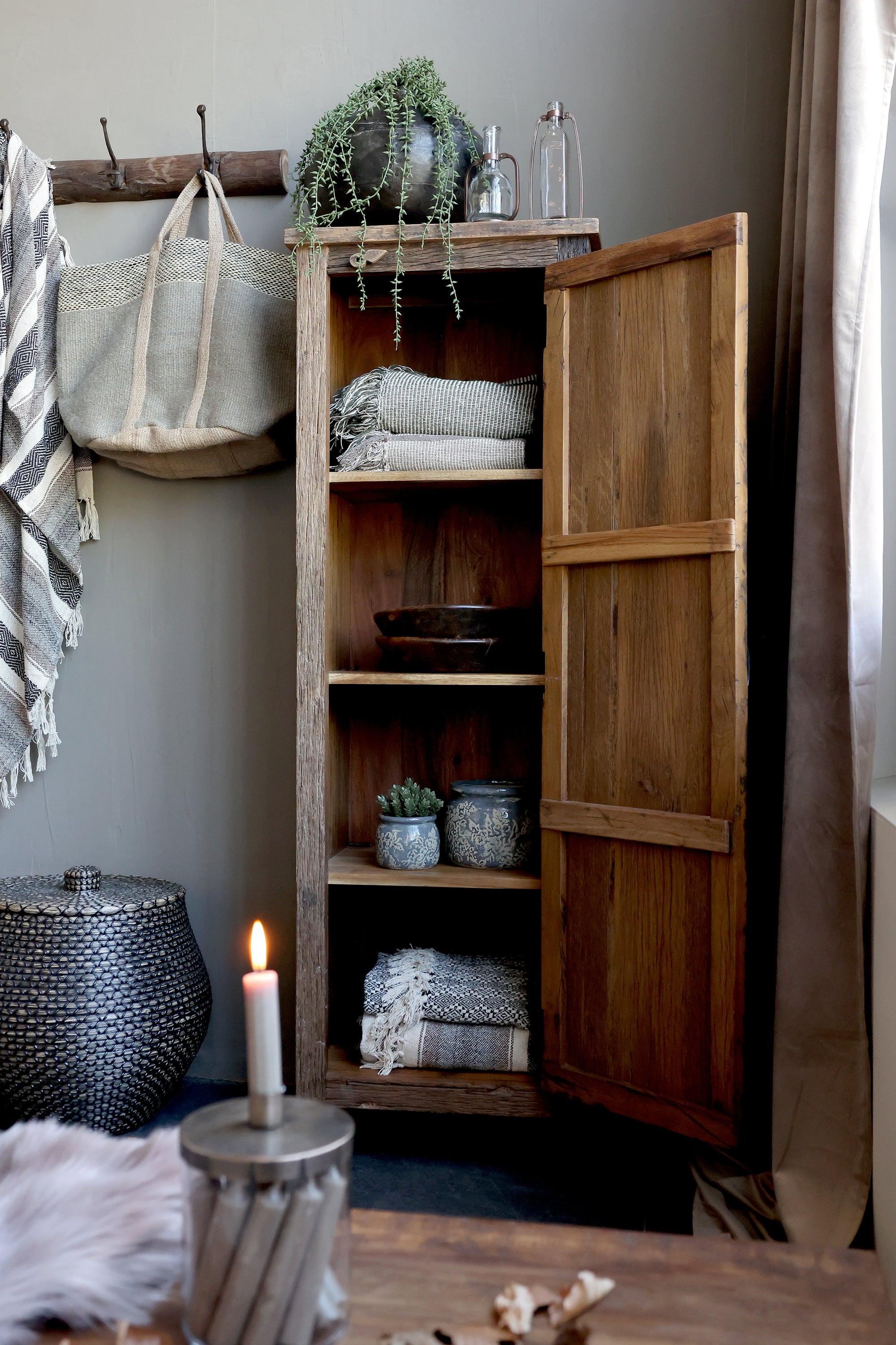 Reclaimed wooden cabinet open filled with blankets, plants and other ornaments.