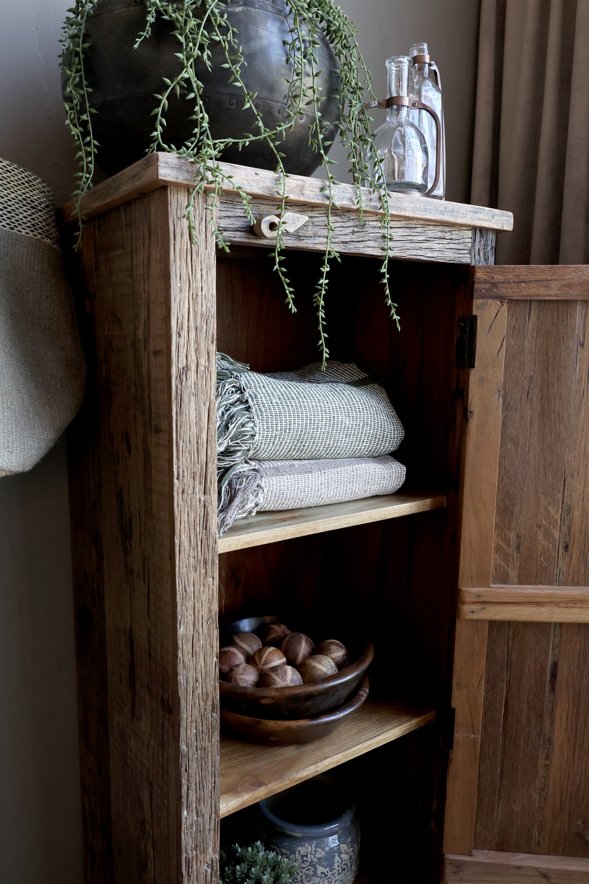 Close up of shelf on reclaimed wooden cabinet, filled with plants, textiles and ornaments.