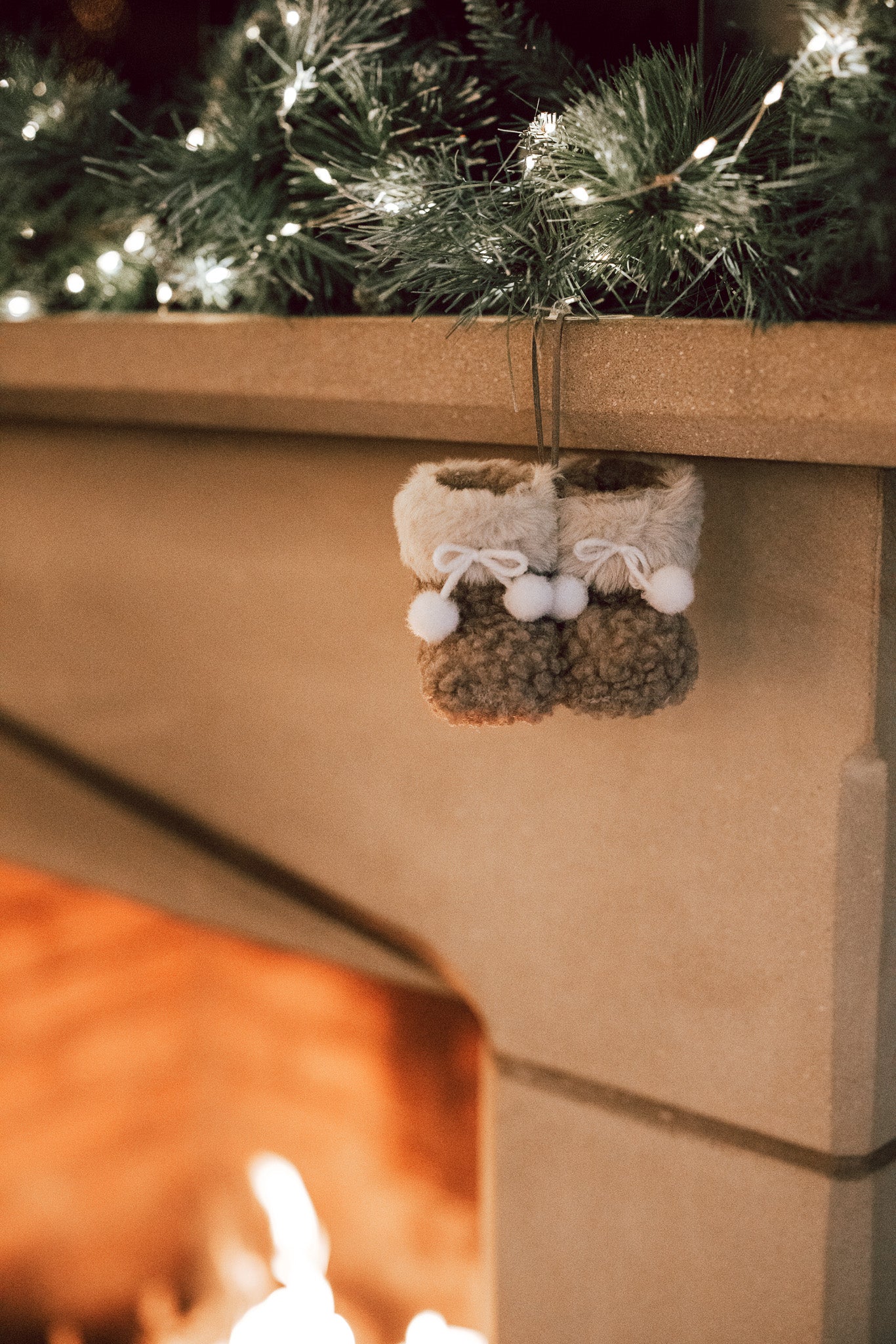 Hanging decoration of brown and white furry booties on stone fireplace with garland.