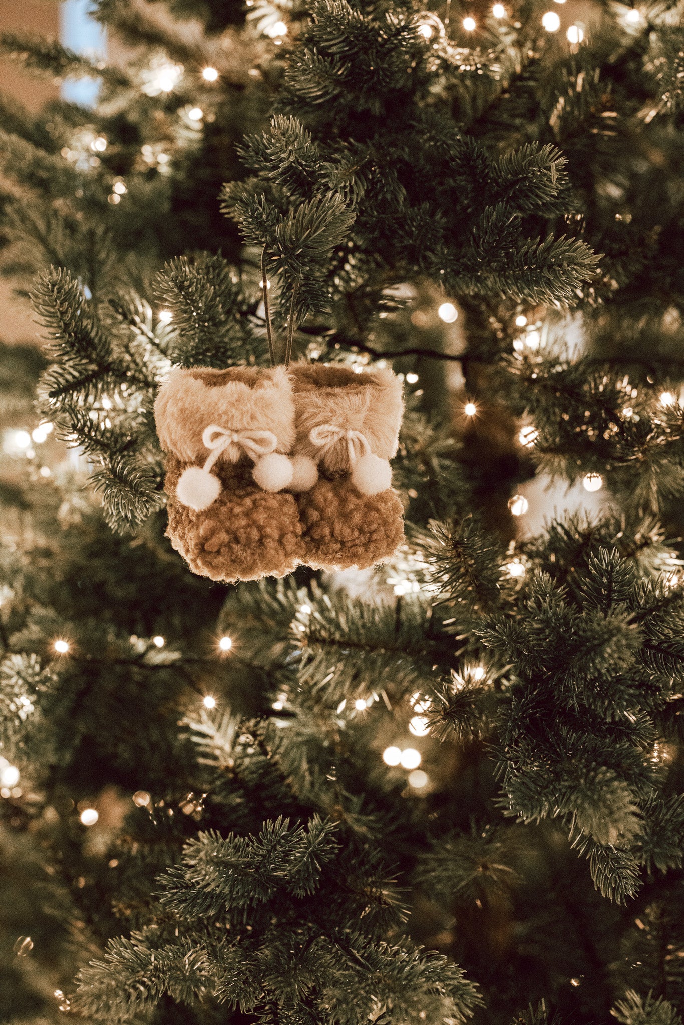 Hanging decoration of brown and white furry booties on Christmas Tree with lights.