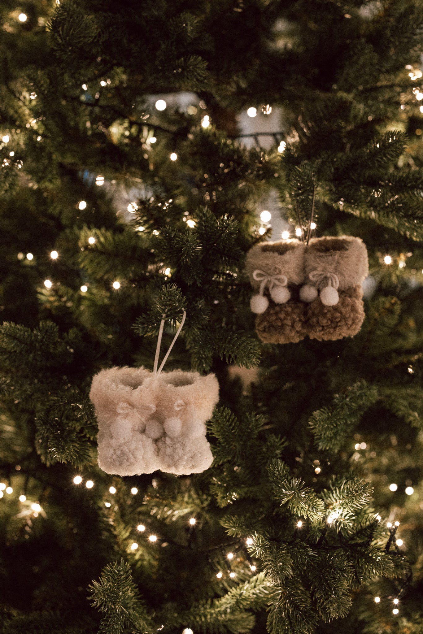 Hanging decoration of brown and white furry booties on Christmas Tree with lights.