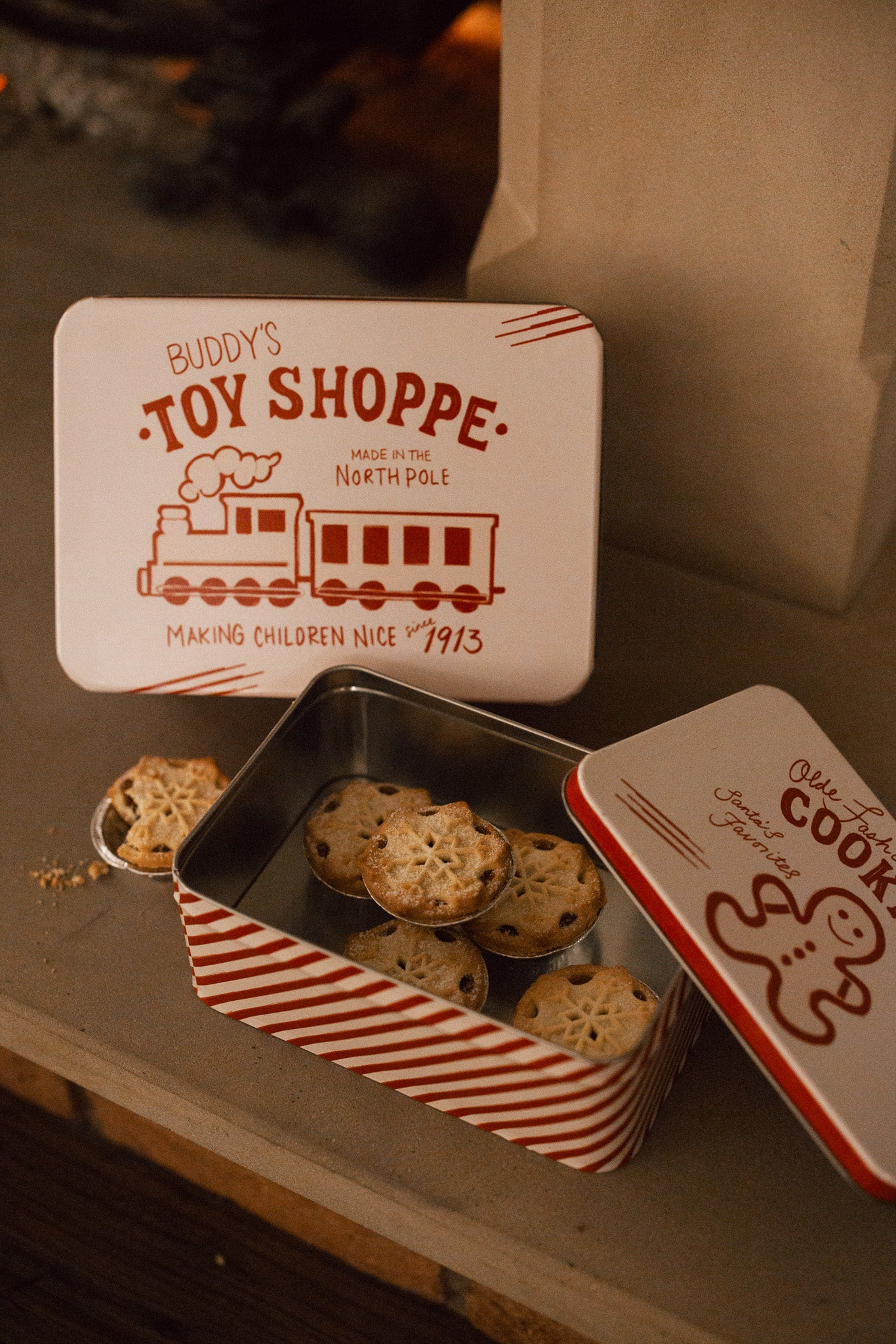 Set of two Christmas themed red and white candy cane storage tins on stone fireplace with a mince pie.