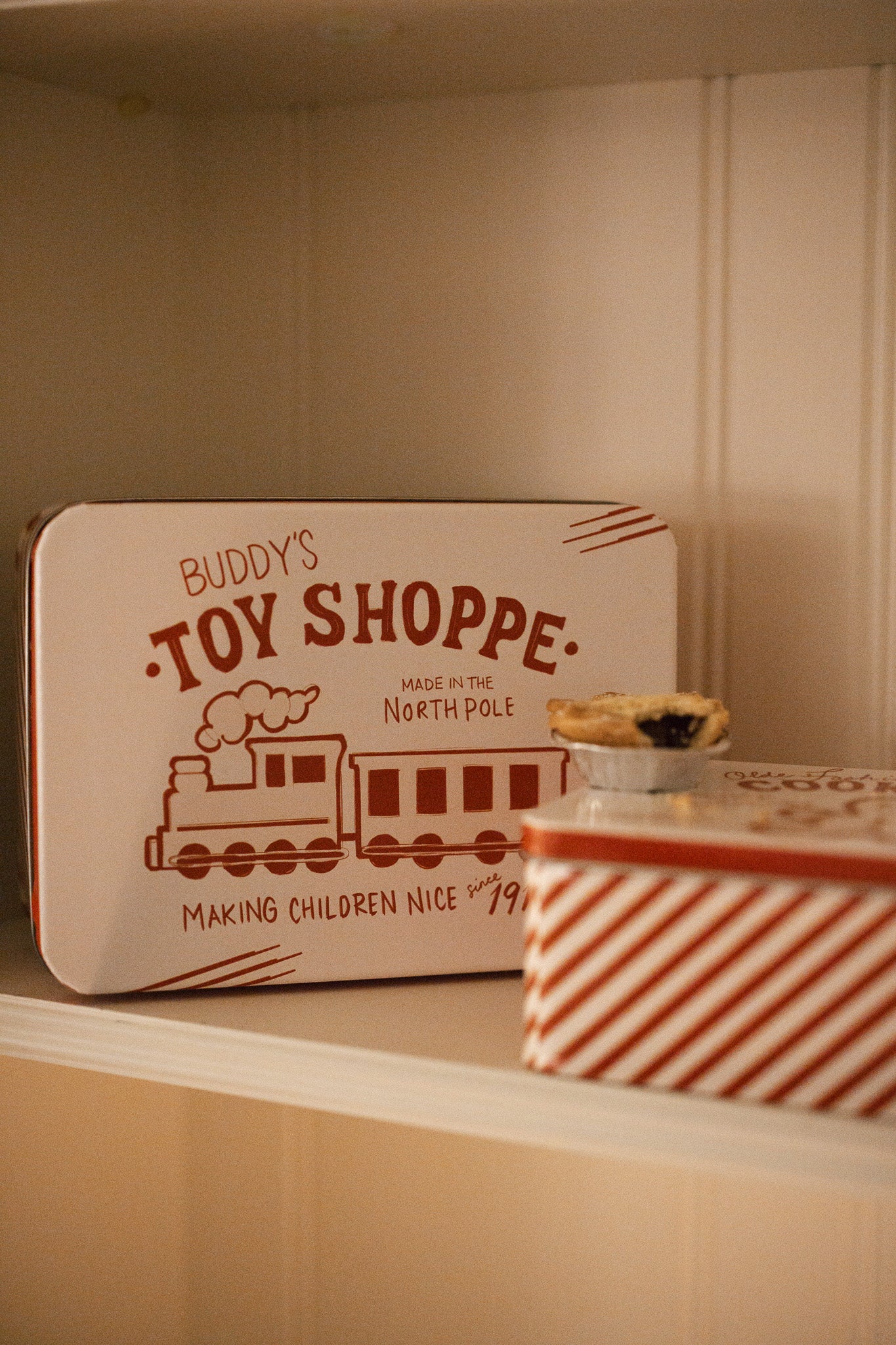 Set of two Christmas themed red and white candy cane storage tins on a white shelf with a mince pie.