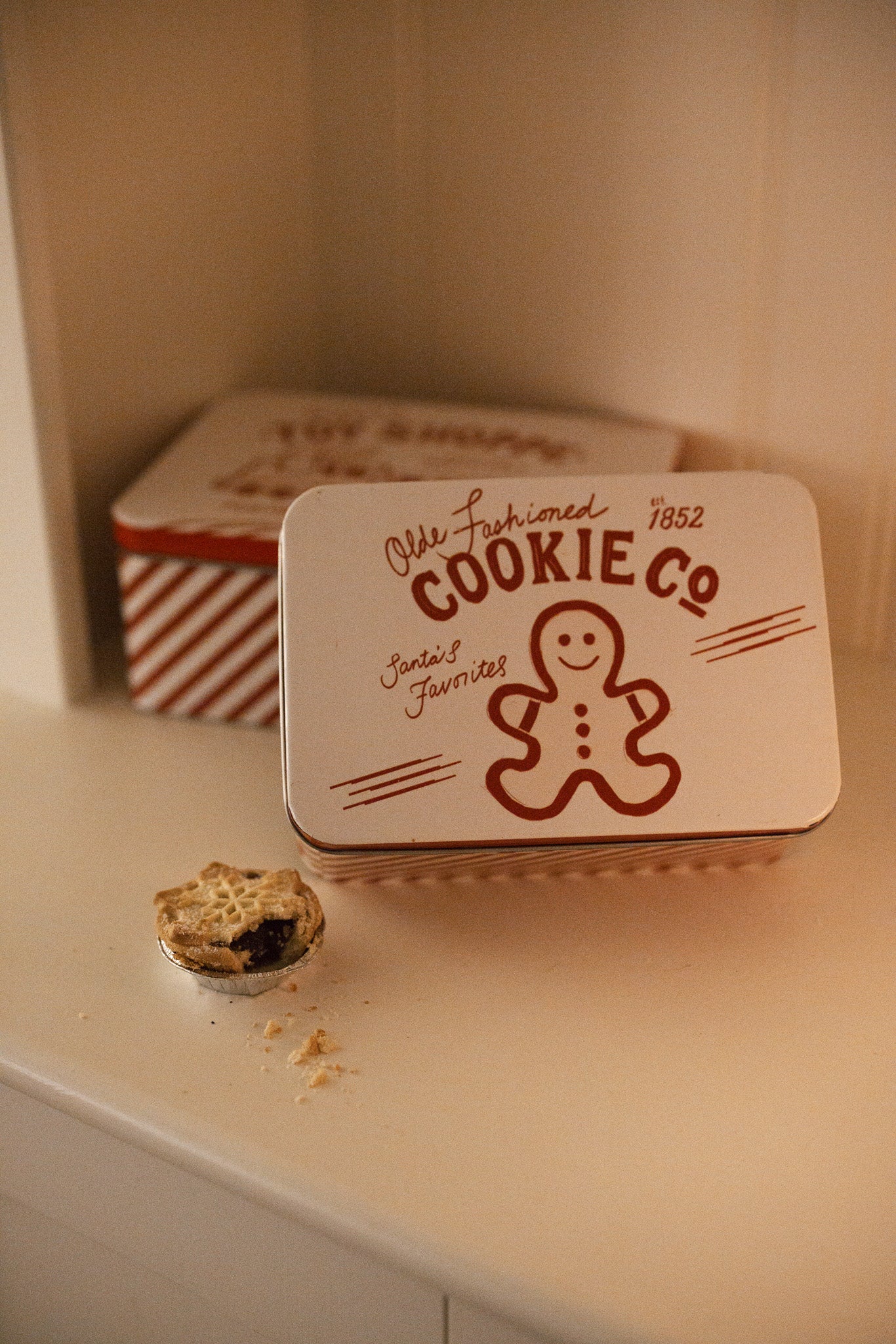 Set of two Christmas themed red and white candy cane storage tins on a white shelf with a mince pie.