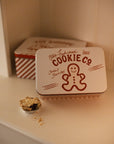 Set of two Christmas themed red and white candy cane storage tins on a white shelf with a mince pie.