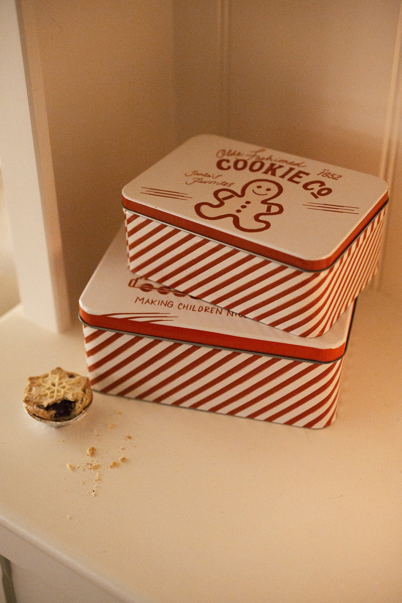 Set of two Christmas themed red and white candy cane storage tins on a white shelf with a mince pie.