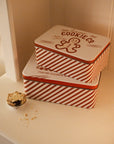 Set of two Christmas themed red and white candy cane storage tins on a white shelf with a mince pie.