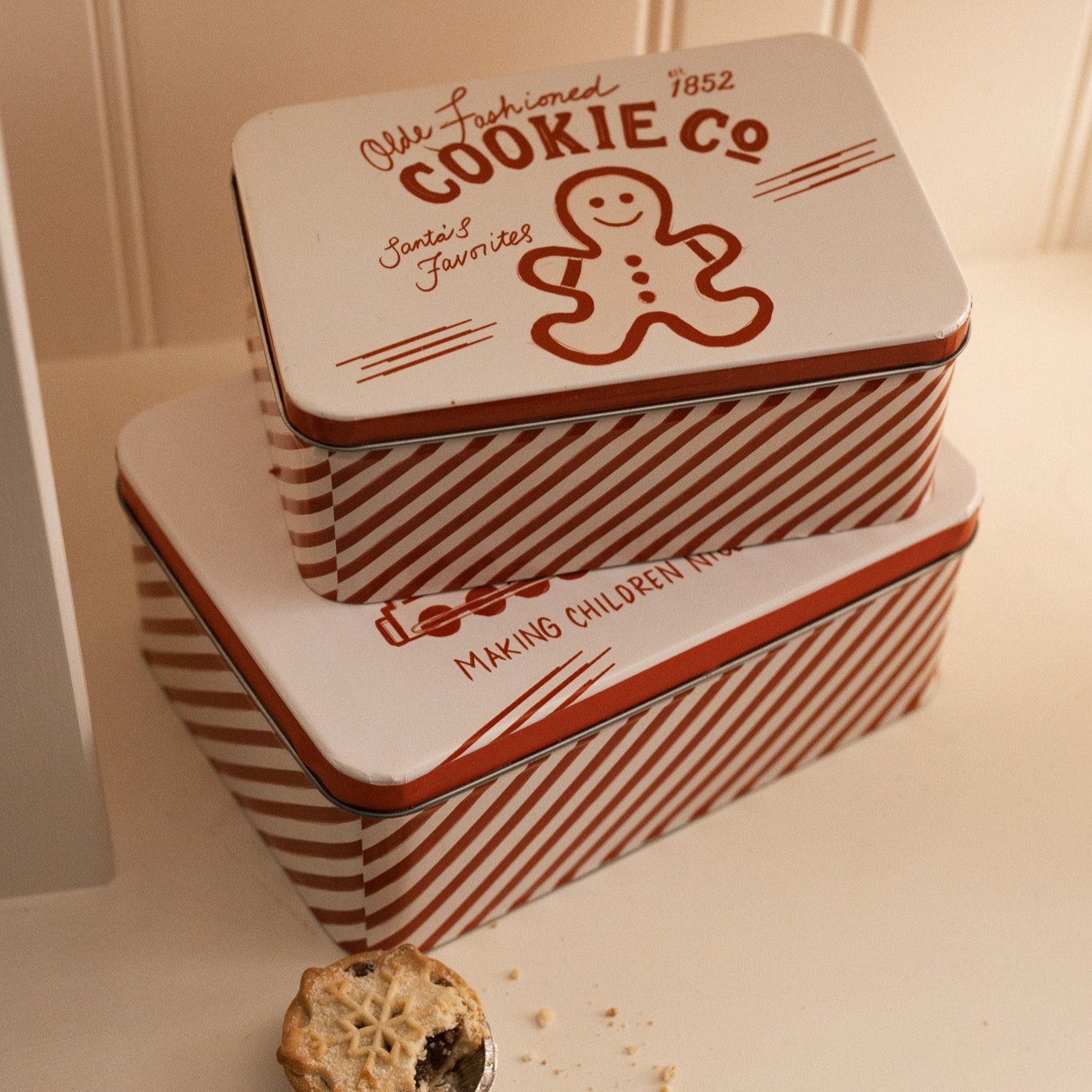 Set of two Christmas themed red and white candy cane storage tins on a white shelf with a mince pie.