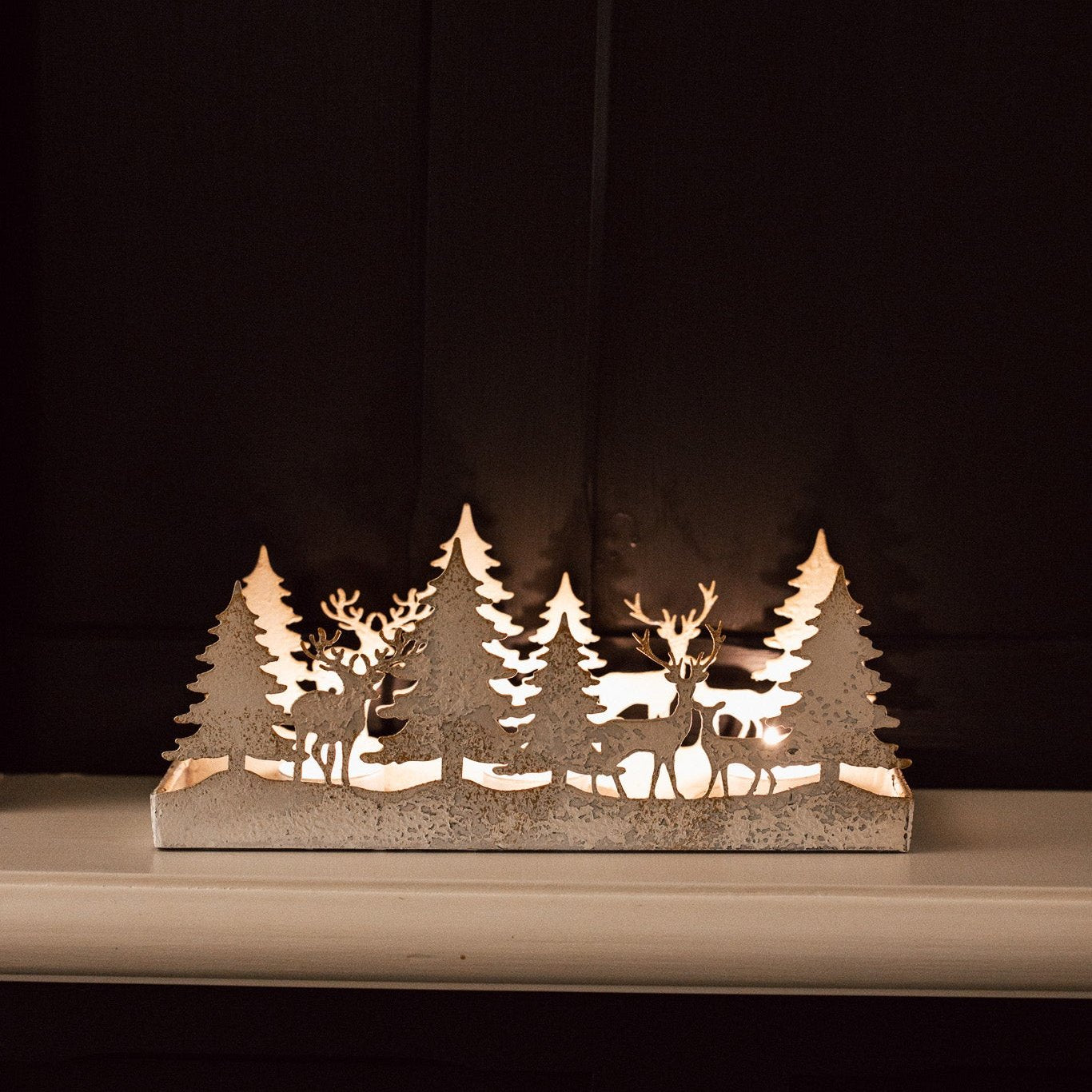 Aged White Reindeer Forest Christmas Holder on black panelled wall.