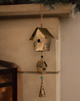 Antiqued brass bird house hanging decoration with two houses, a bell and green beads on stone fire place.