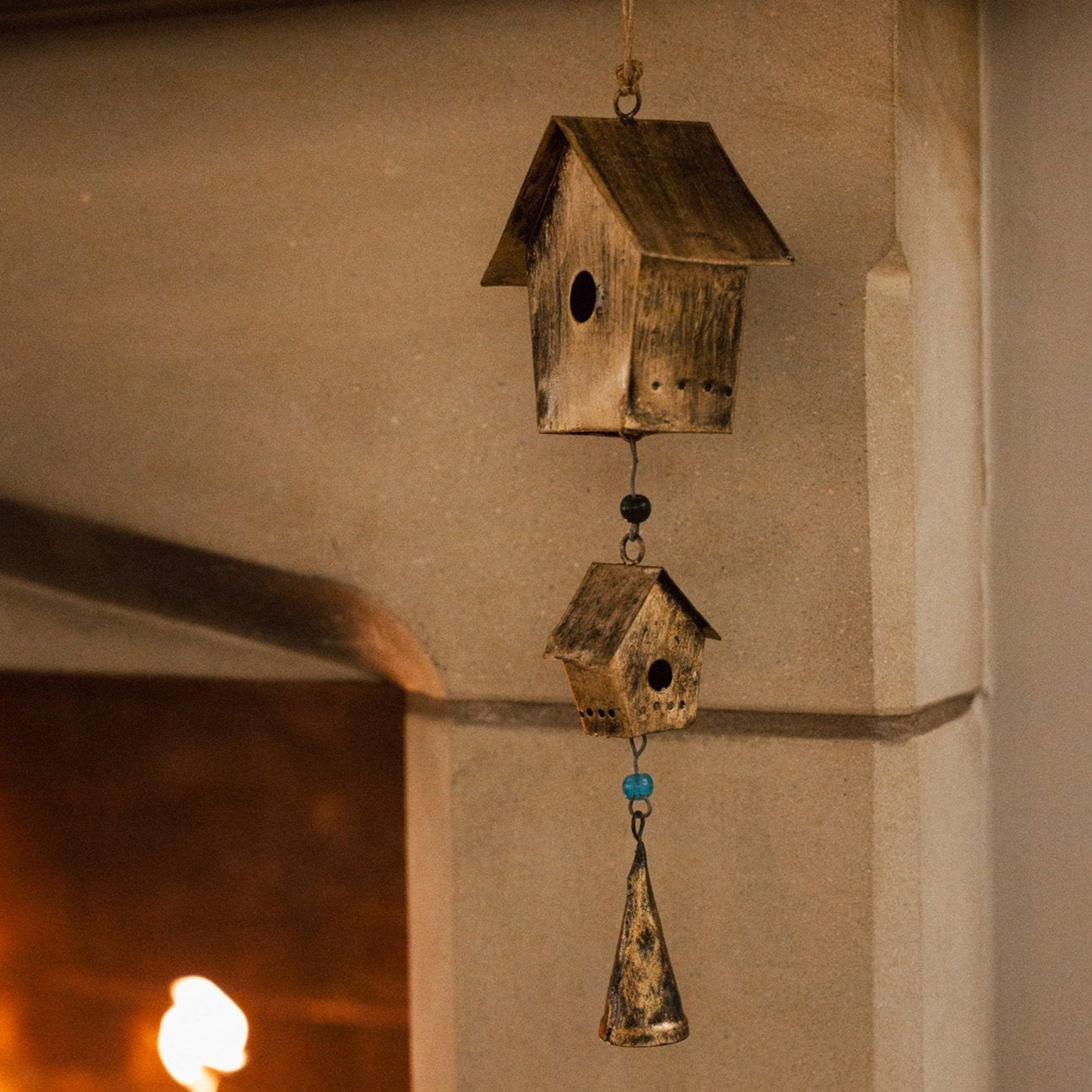 Antiqued brass bird house hanging decoration with two houses, a bell and green beads on stone fire place.