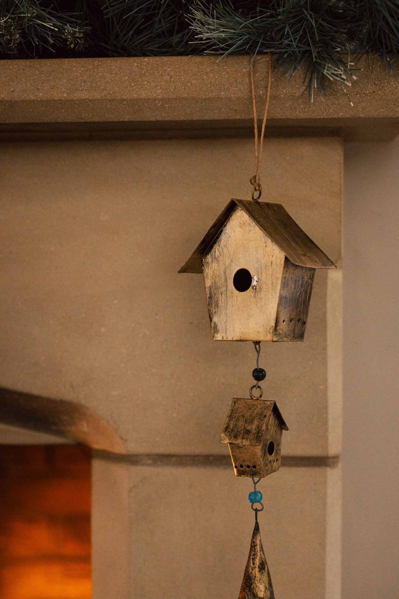 Antiqued brass bird house hanging decoration with two houses, a bell and green beads on stone fire place.