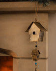 Antiqued brass bird house hanging decoration with two houses, a bell and green beads on stone fire place.