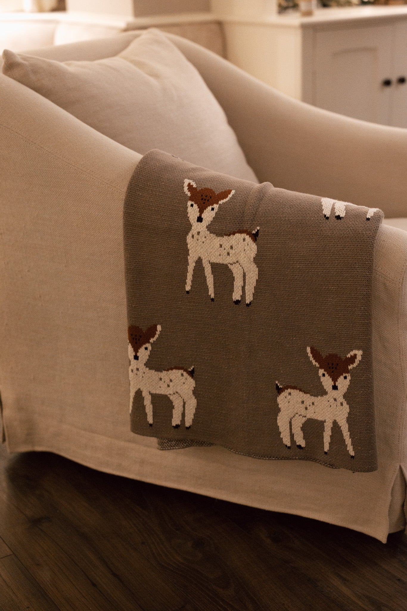 Neutral Christmas throw with Bambi reindeer print folded up on the arm of an armchair.