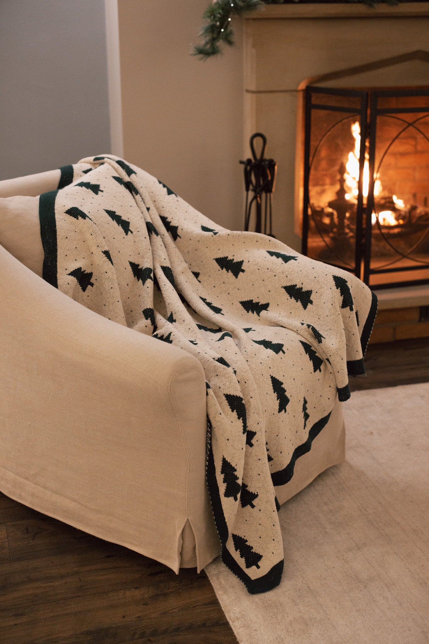 White cotton throw with Christmas tree and polkadot pattern with green border, draped over a cream armchair.