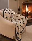 White cotton throw with Christmas tree and polkadot pattern with green border, draped over a cream armchair.