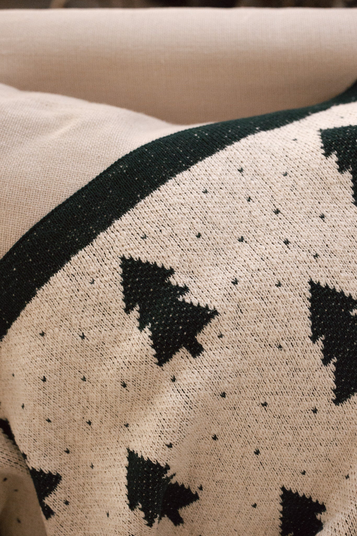 White cotton throw with Christmas tree and polkadot pattern with green border, draped over the back of a cream armchair.