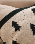 White cotton throw with Christmas tree and polkadot pattern with green border, draped over the back of a cream armchair.