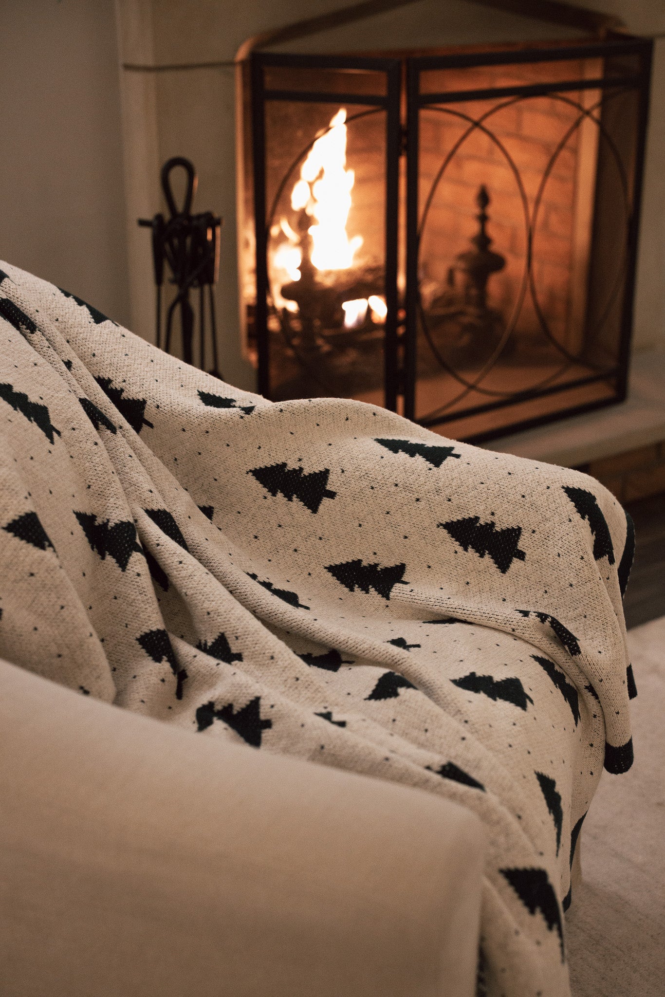 White cotton throw with Christmas tree and polkadot pattern with green border, draped over the arm of a cream armchair.