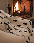 White cotton throw with Christmas tree and polkadot pattern with green border, draped over the arm of a cream armchair.