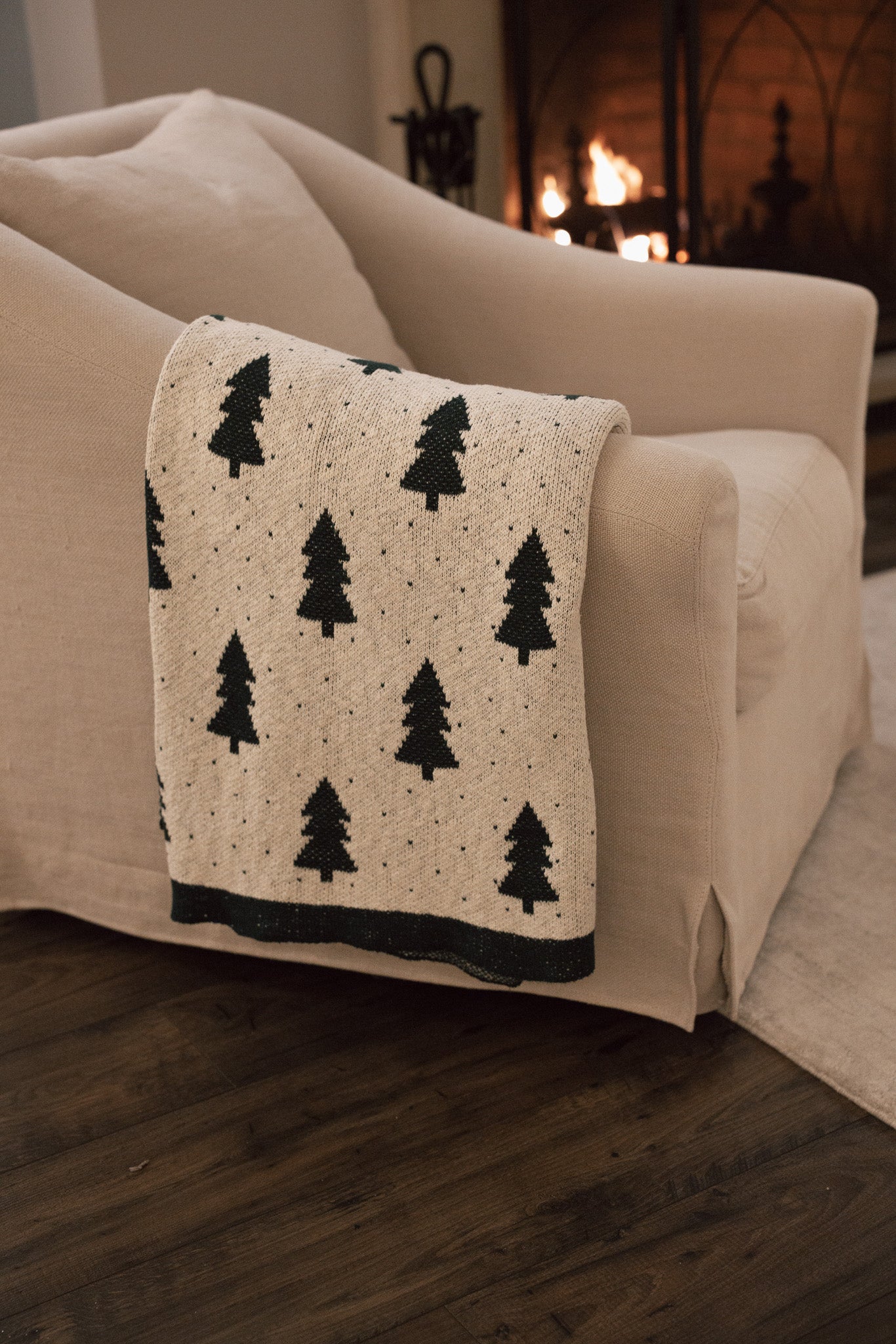 White cotton throw with Christmas tree and polkadot pattern with green border, draped over the arm of a cream armchair.