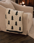 White cotton throw with Christmas tree and polkadot pattern with green border, draped over the arm of a cream armchair.