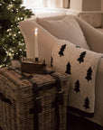 A rattan storage box side table with candle stick and christmas tree throw in front of lit up christmas Tree.