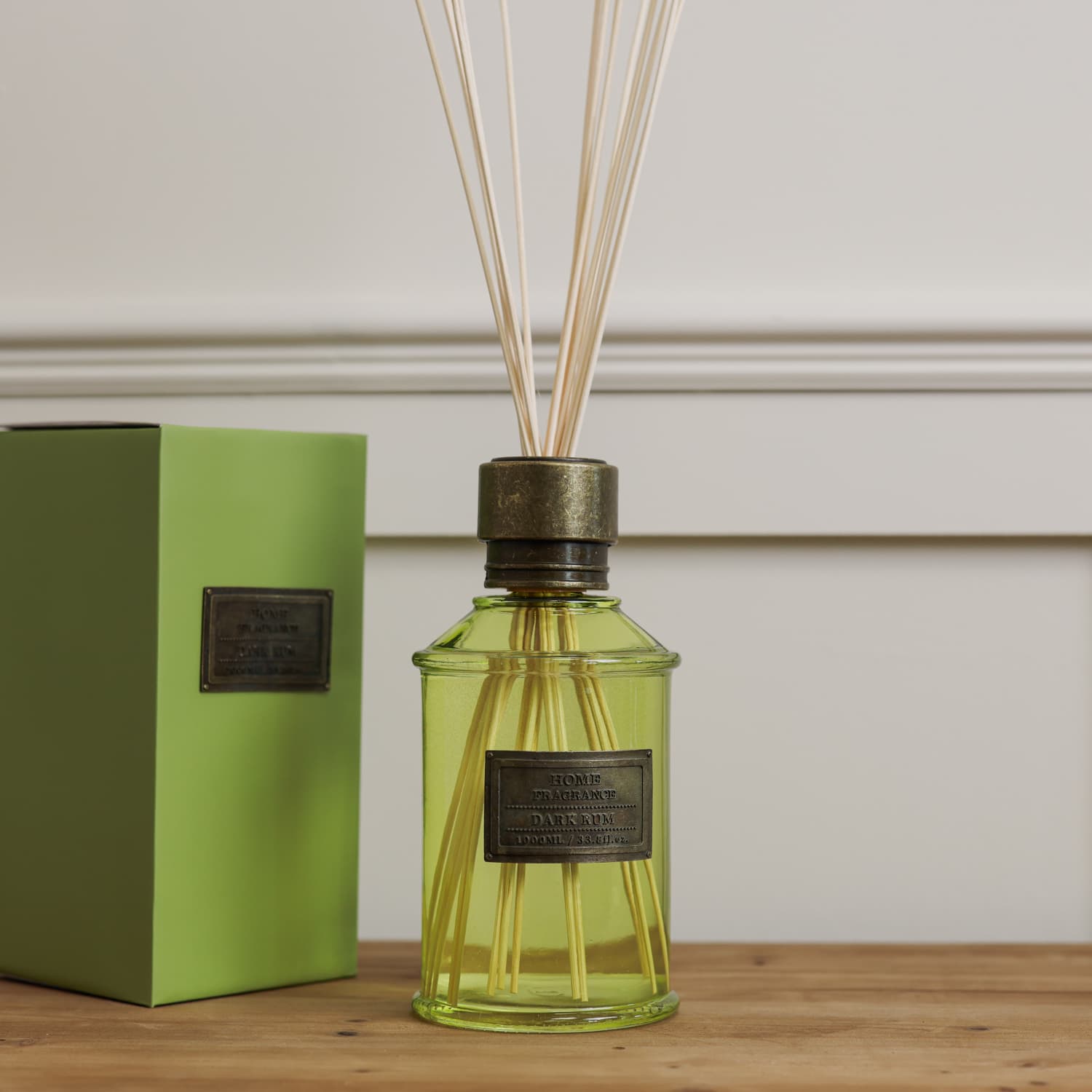 Home fragrance dark rum and lime green reed diffuser on wooden console with presentation box