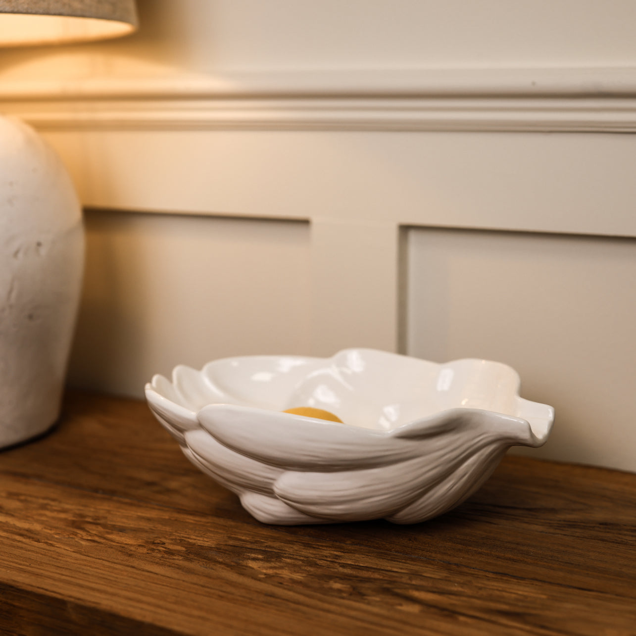 White artichoke ceramic bowl with lemon in on wooden console.