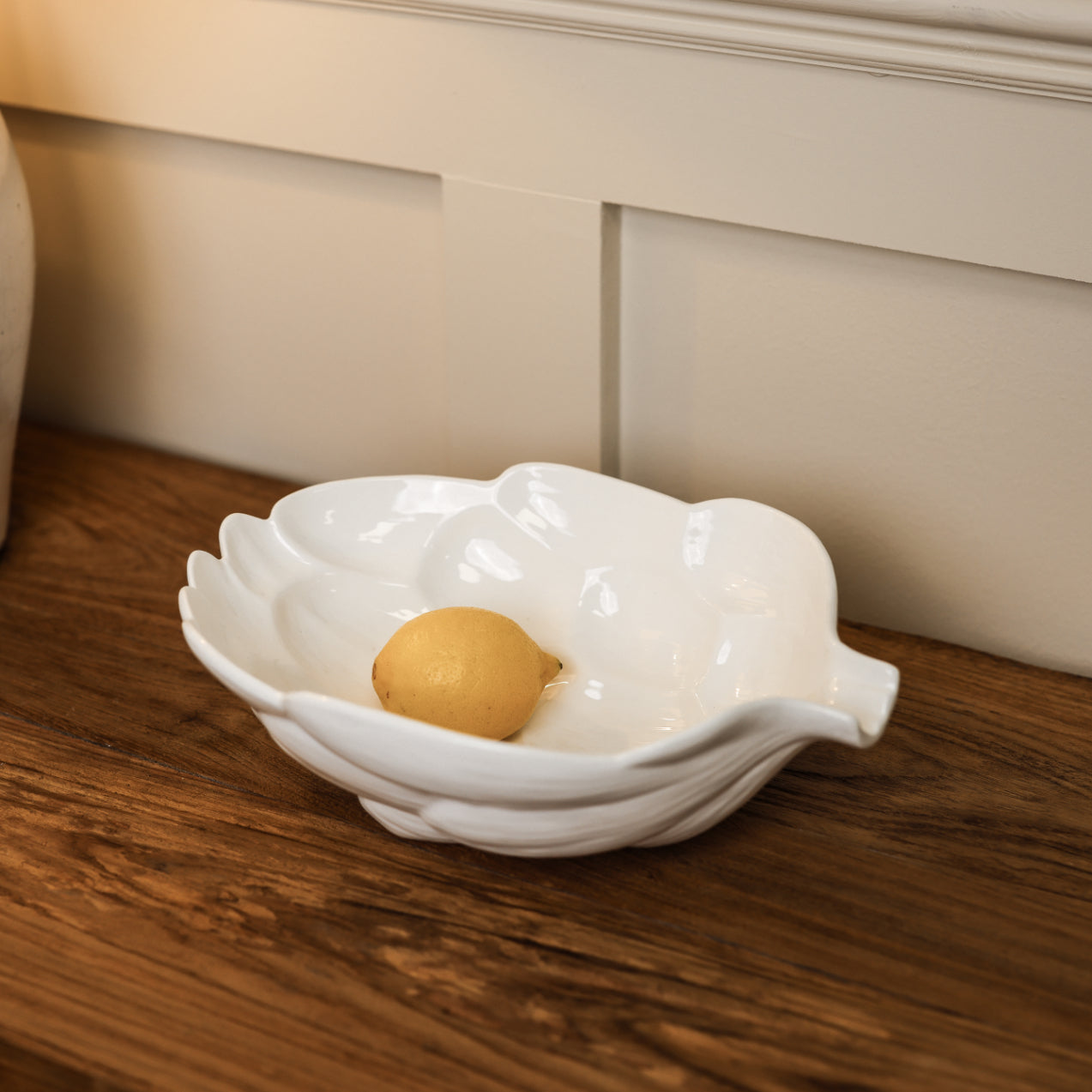 White artichoke ceramic bowl with lemon in on wooden console.