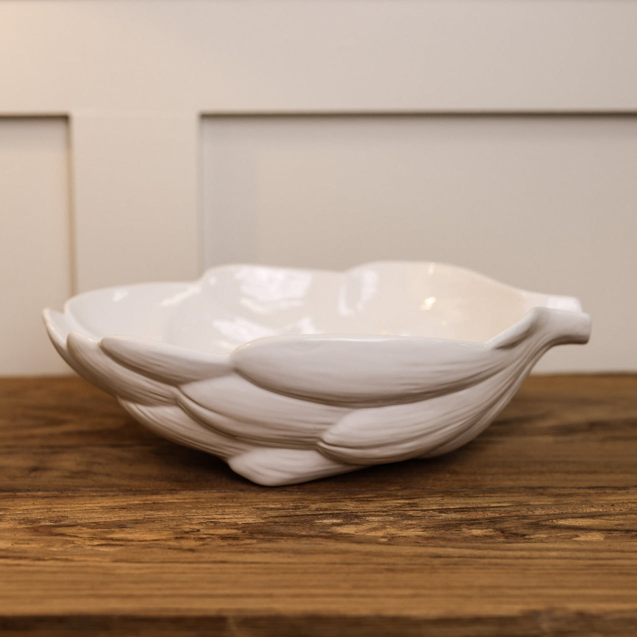 White artichoke ceramic bowl from side view, on wooden console.