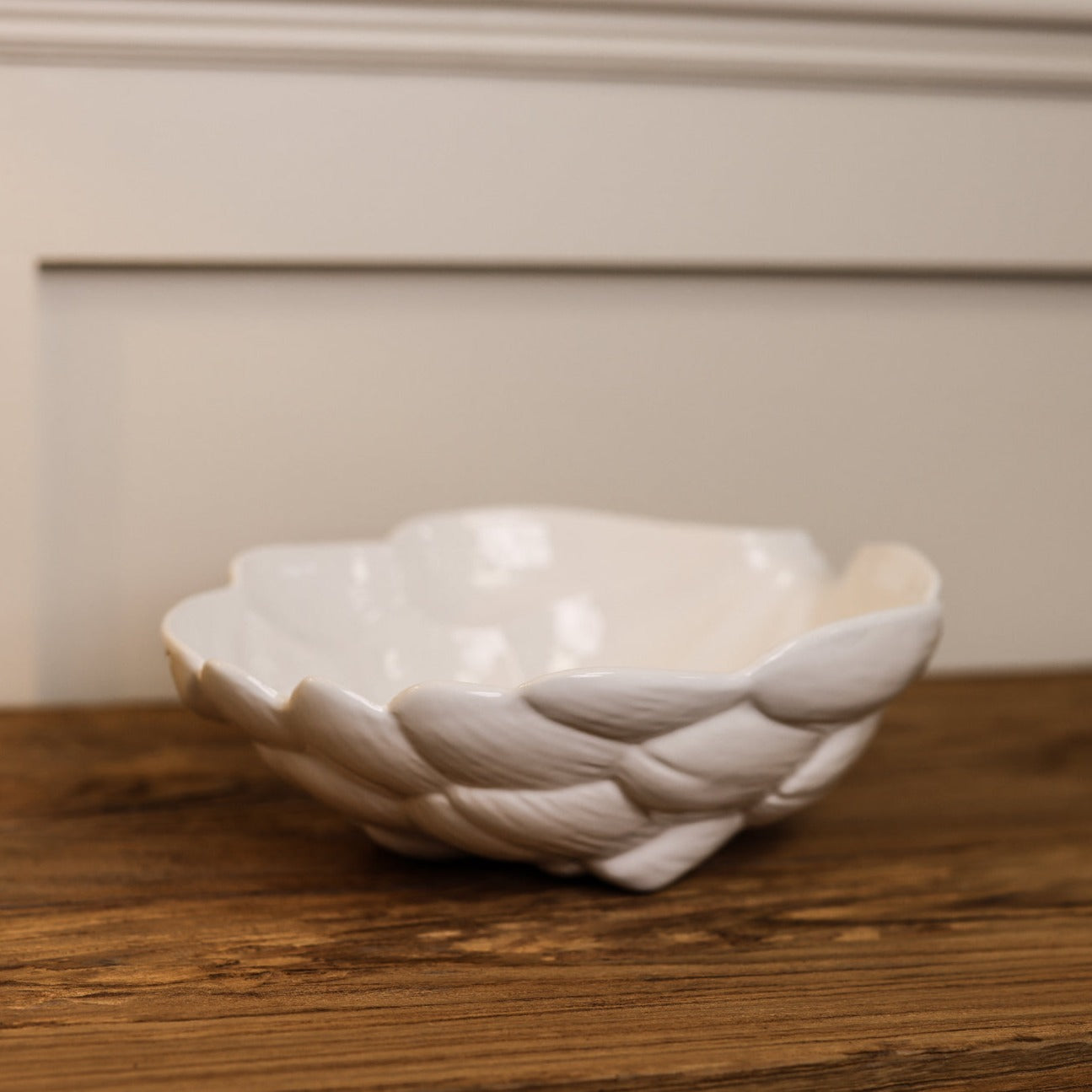 Side view of white artichoke ceramic bowl on wooden console.