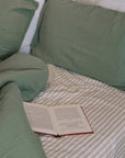 unmade green and striped bedding with an open book.