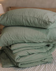 Folded green muslin bedding on striped bedsheet.