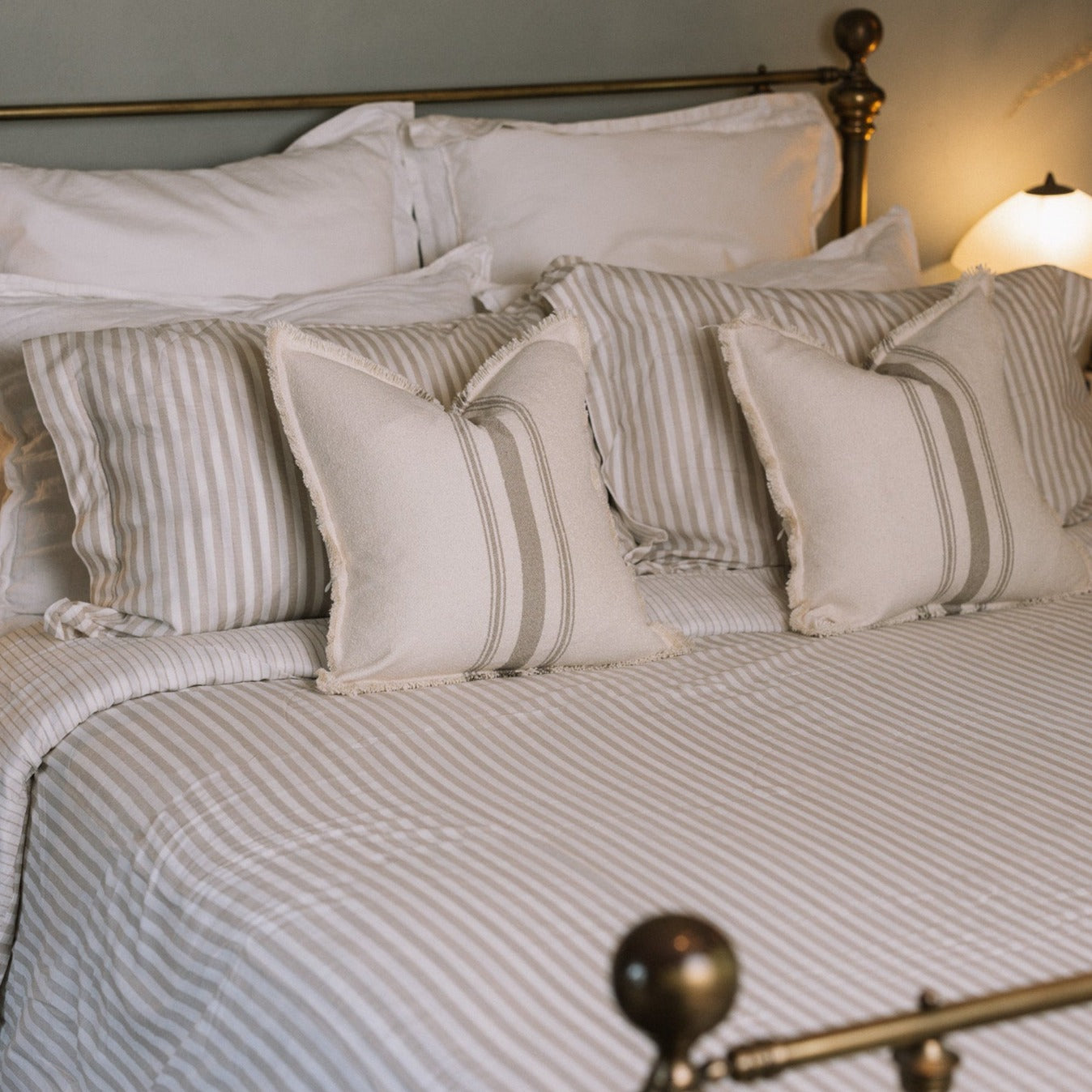 Striped neutral bedding on a brass bed.