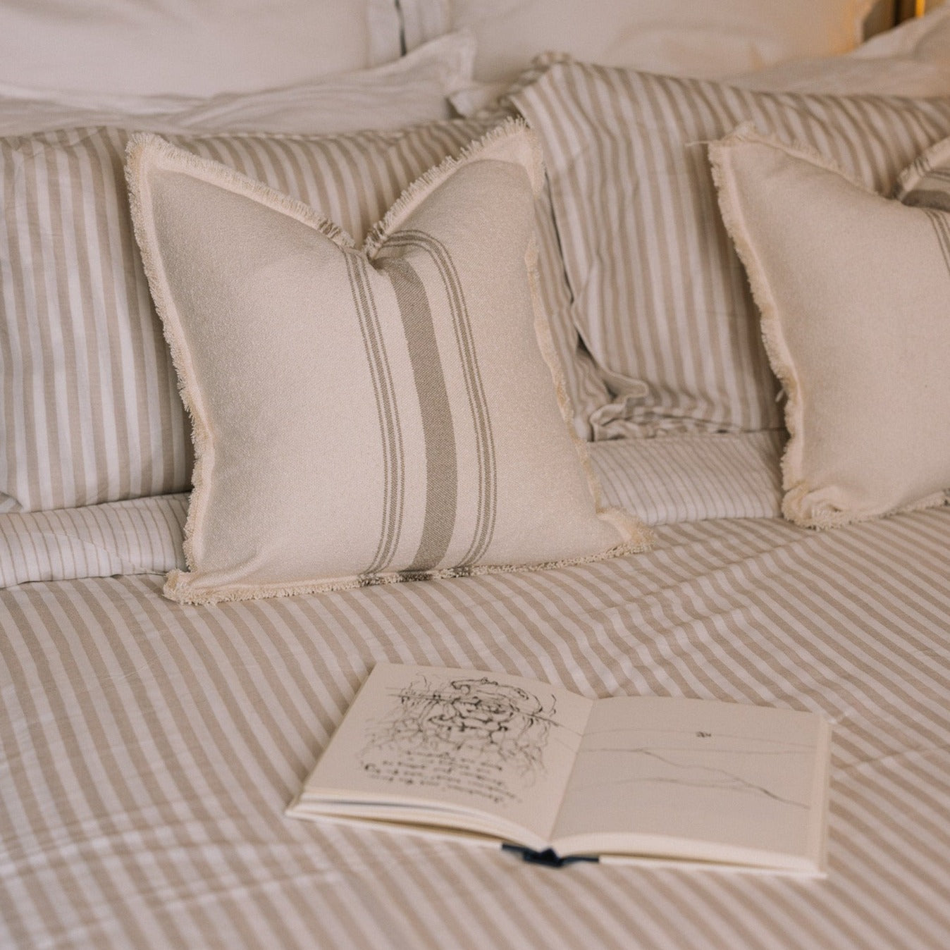 Striped neutral bedding on a brass bed with an open book.